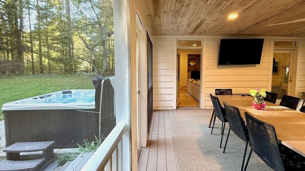 Un espace extérieur abrité comprenant un jacuzzi, une table à manger avec des chaises et un téléviseur fixé au mur.