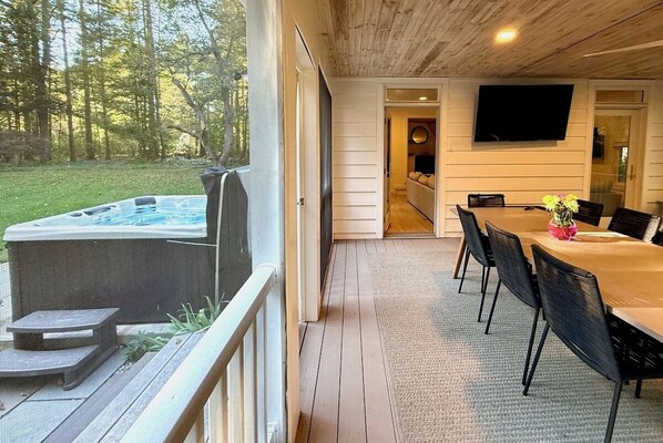 A covered outdoor area with a hot tub, a dining table with chairs, and a TV mounted on the wall.