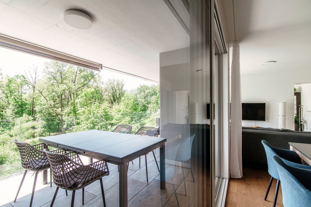 A modern living space with a balcony, a dining area with chairs, and a kitchen area with a TV.