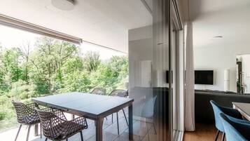 Un espacio de estar moderno con balcón, zona de comedor con sillas y área de cocina con televisor.