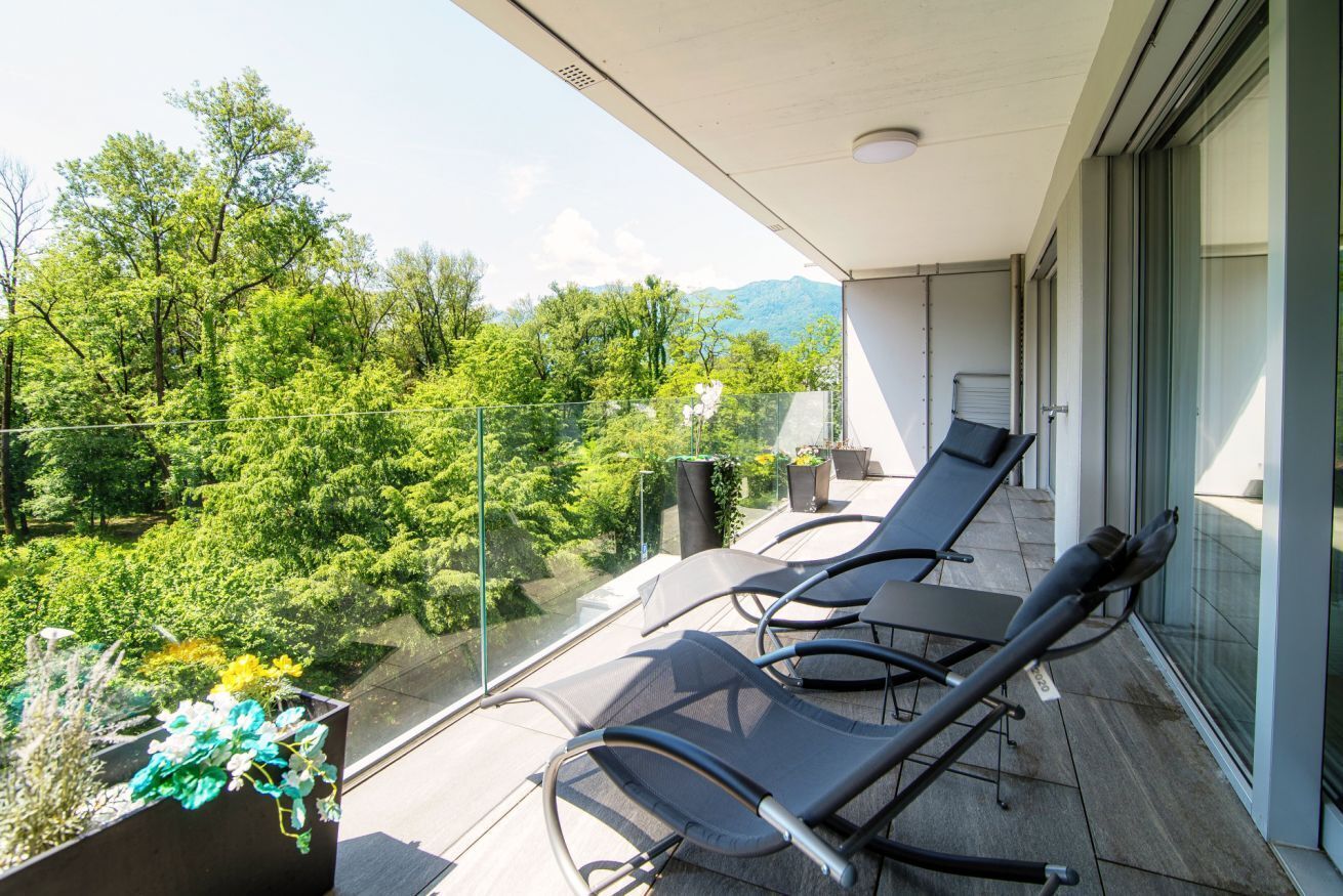 Un balcon avec deux fauteuils de jardin, une balustrade en verre et une vue sur une zone boisée.