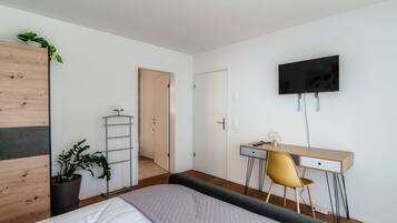 A bedroom with a bed, a desk, a chair, a TV, and a potted plant.