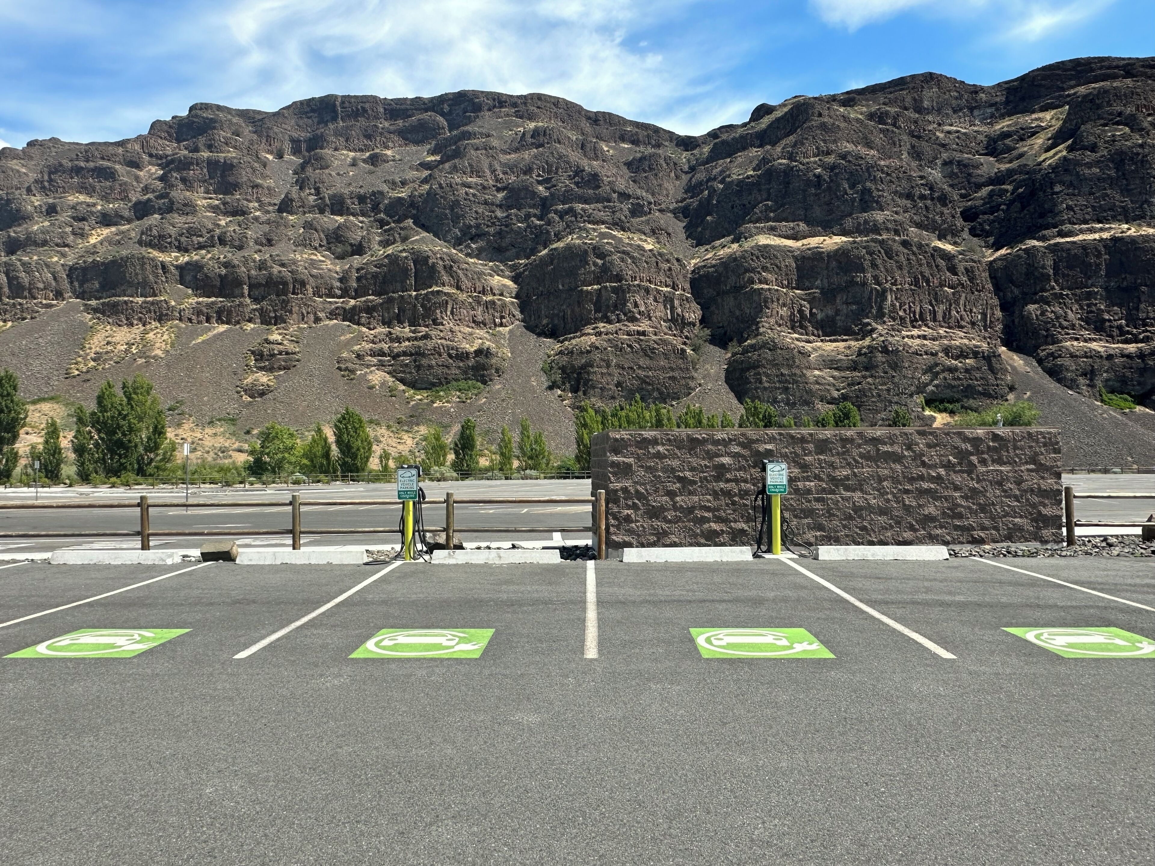 A parking lot with electric vehicle charging stations, marked parking spaces, and a view of rocky mountains in the background.