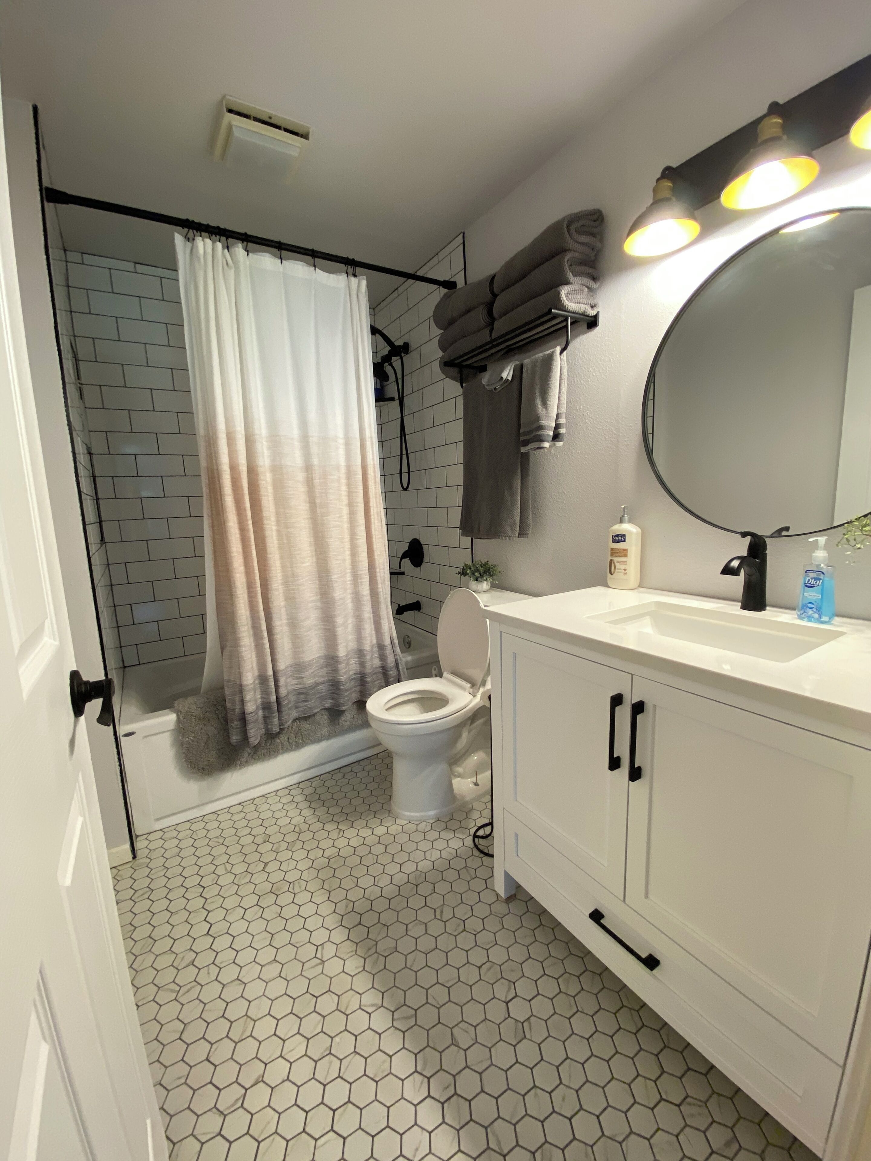 A bathroom with a white sink, a toilet, a shower with a curtain, and a mirror with lights.