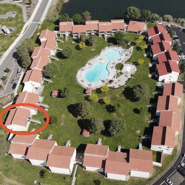 An aerial view of a residential area with a central swimming pool surrounded by houses with red roofs.