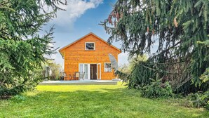 Une cabane en bois avec une porte d’entrée, une petite fenêtre et une terrasse aménagée avec du mobilier d’extérieur.