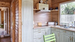 Une cuisine de taille réduite, dotée de meubles en bois, d’une fenêtre ornée de rideaux en dentelle et d’une chaise verte.