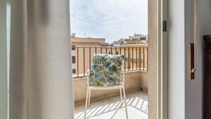 Un balcon avec une chaise blanche et un coussin, donnant sur un paysage urbain avec des immeubles.