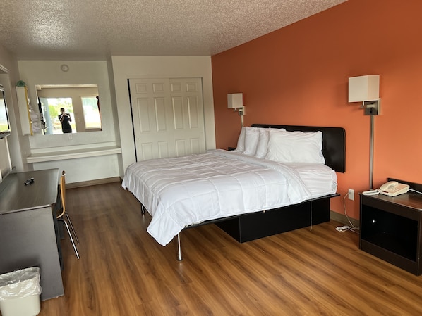A hotel room with a bed, bedside table, lamp, and a desk with a chair. - LAKE INN (Buckeye Lake)