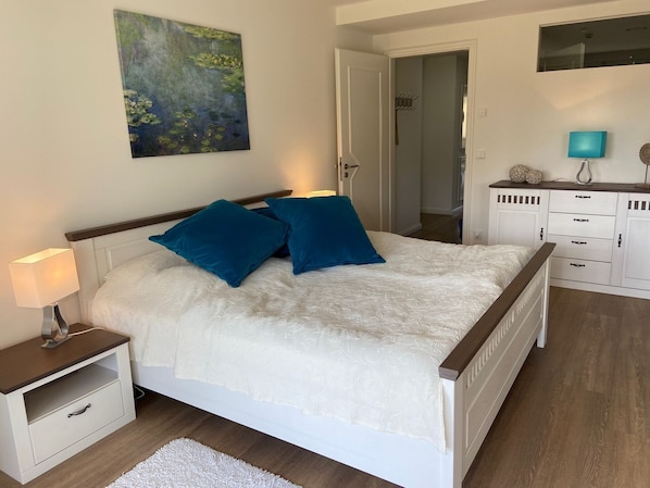Quarto com cama, mesa de cabeceira, penteadeira, espelho e um quadro na parede.