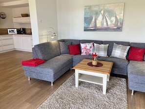 Uma sala de estar moderna com um sofá seccional cinza, uma mesa de centro de madeira e uma pintura de veleiros na parede.