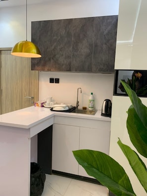 Una cocina compacta con diseño moderno, que incluye una encimera blanca, un lavamanos empotrado y una lámpara colgante.