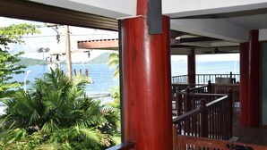 A wooden balcony with a view of the sea and a lush green plant in the foreground. - Kalim Résidence unit- 133 (Patong)
