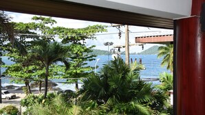 A view from a window overlooking a beach with palm trees and a body of water. - Kalim Résidence unit- 133 (Patong)