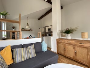 A modern living room with a dark grey sofa, wooden cabinets, and a kitchen in the background. - Haus Möwe - Ferienwohnung 5 "heringsmöwe" - Lietzow Appartementhaus Möwe (Lietzow)