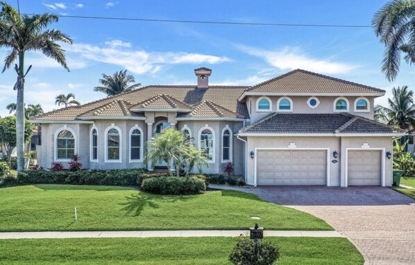 A two-story house with a tiled roof, a garage, and a well-maintained lawn with palm trees. - Beautiful Marco island executive home on the water (Marco Island)