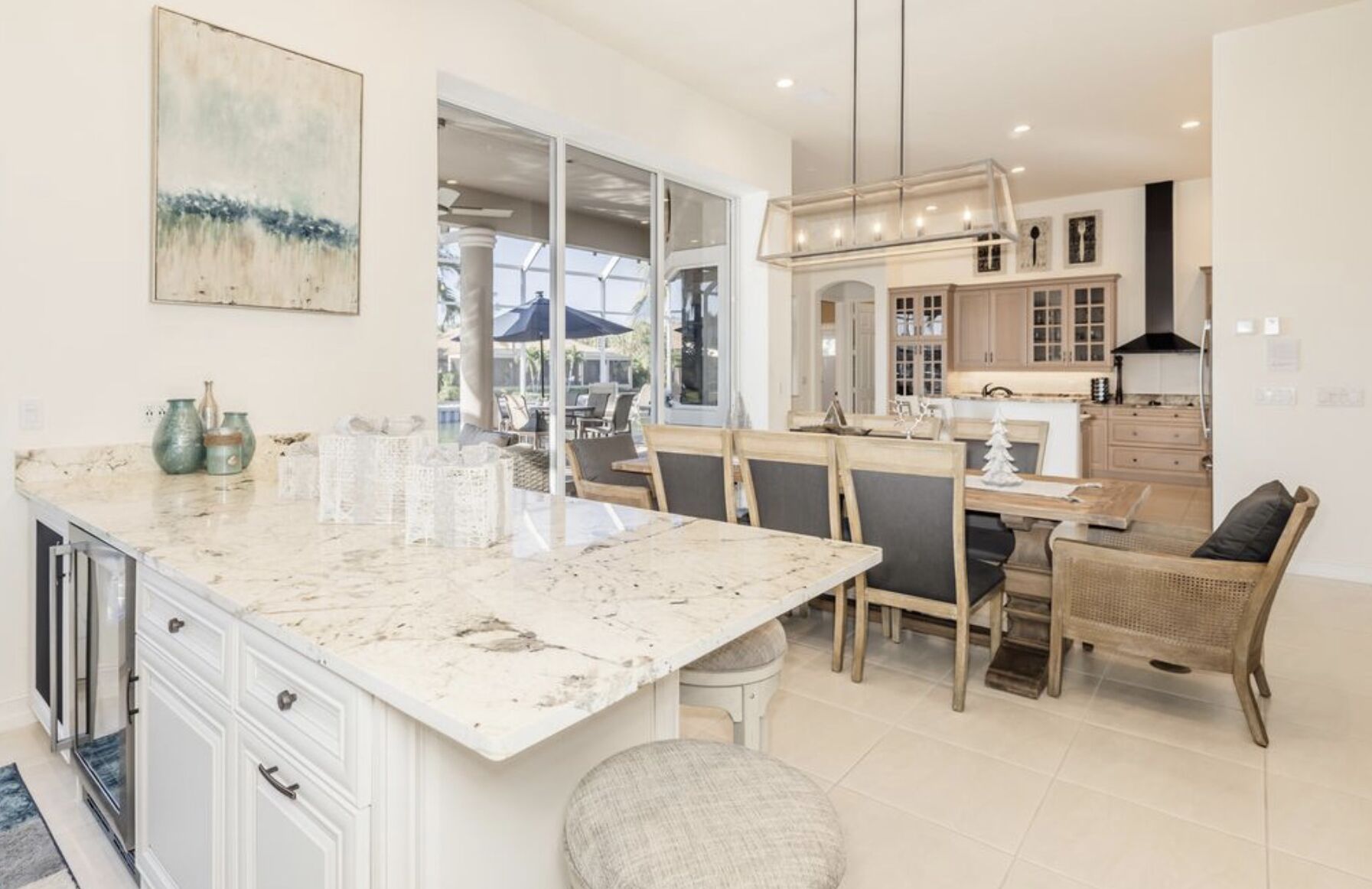 A modern kitchen with a marble countertop, white cabinetry, and a dining area with wicker chairs.