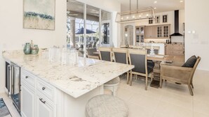 Een moderne keuken met een marmeren aanrechtblad, witte kasten en een eethoek met rieten stoelen.