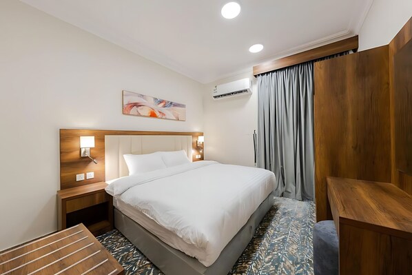 Una habitación de hotel con una cama grande, cabecera de madera, lámparas de noche, un cuadro en la pared y un banco de madera.