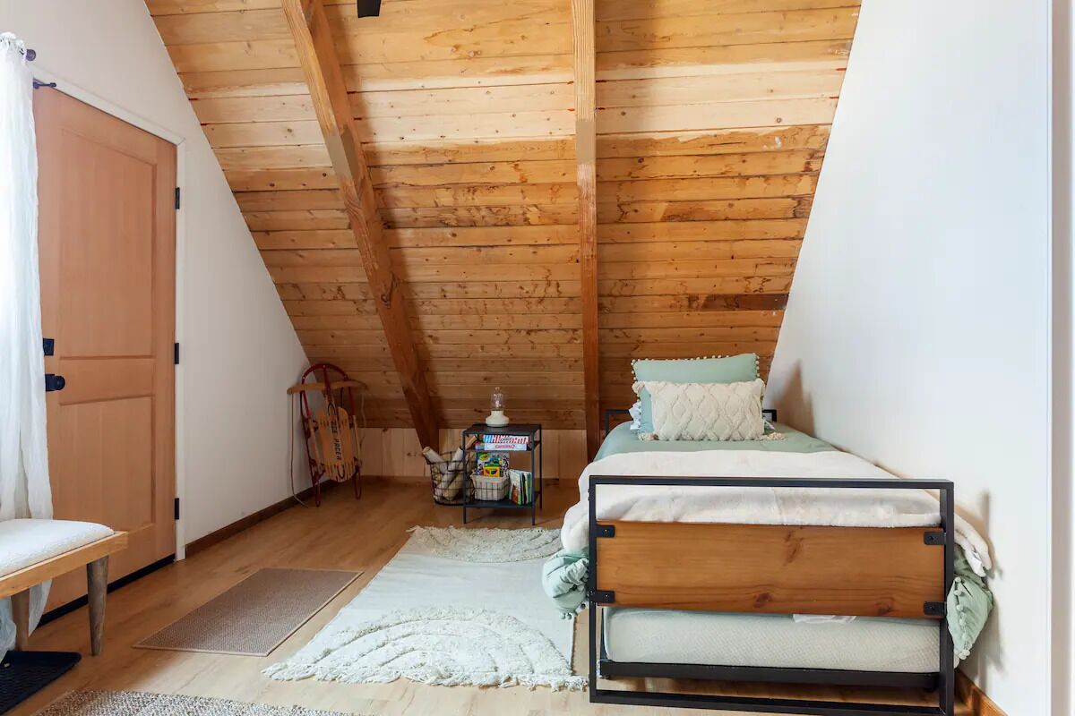 A cozy attic bedroom with a sloped ceiling, a wooden bed, a small desk, and a chair.