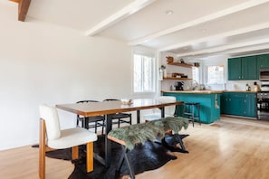Une cuisine moderne avec des meubles de couleur turquoise, une table à manger en bois et un banc noir à la texture duveteuse.