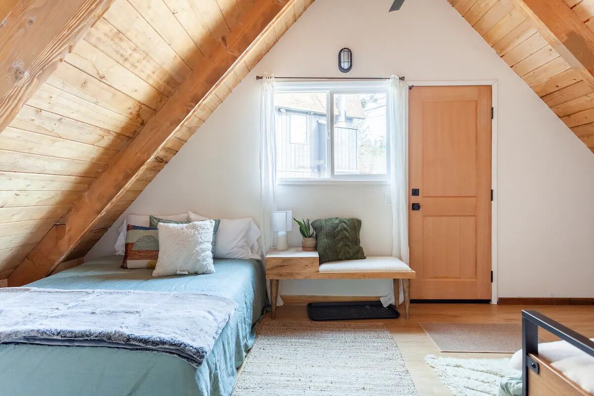 Une chambre mansardée chaleureuse, avec un plafond en pente, un lit, un banc, une fenêtre et une porte.