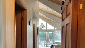 A spacious hallway with wooden flooring and large sliding doors leading to a balcony with a view of a lake. - Over water Beach house with pickleball  (MacTier)
