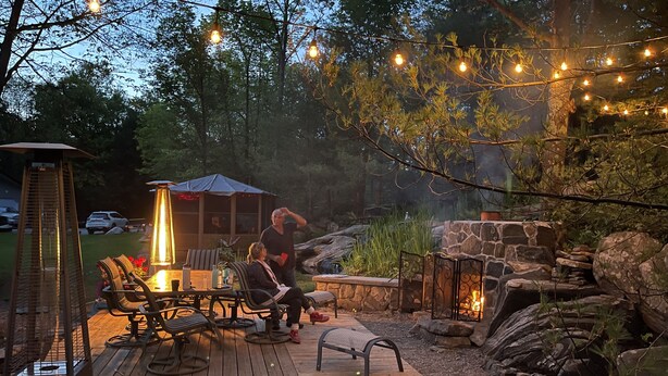 A wooden deck with outdoor furniture, a stone fire pit, and string lights. - Over water Beach house with pickleball  (MacTier)