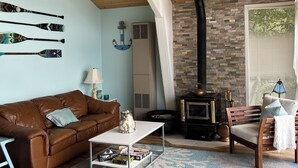A cozy living room with a brown leather sofa, a coffee table, and a fireplace with a stone wall. - Over water Beach house with pickleball  (MacTier)