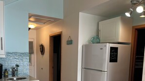 A kitchen with white cabinets, a marble countertop, a white refrigerator, and a hanging light fixture. - Over water Beach house with pickleball  (MacTier)