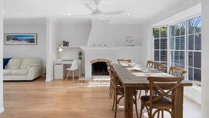 A modern dining area with a wooden table and chairs, a fireplace, and a view of the outdoors through large windows. - Beach House With Pool, Pets Welcome! (Coolum Beach)