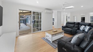 A modern living room with a black leather sofa, a wooden coffee table, and a sliding glass door leading to a balcony. - Beach House With Pool, Pets Welcome! (Coolum Beach)