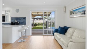 A modern kitchen with a white countertop, bar stools, and a view of the backyard through glass doors. - Beach House With Pool, Pets Welcome! (Coolum Beach)