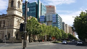Una calle con edificios modernos e históricos, incluyendo una torre destacada y un edificio con fachada de vidrio y señalización.