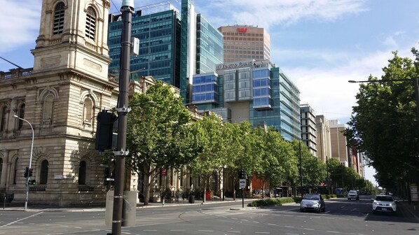 A street with modern and historic buildings, including a prominent tower and a glass-fronted building with signage.