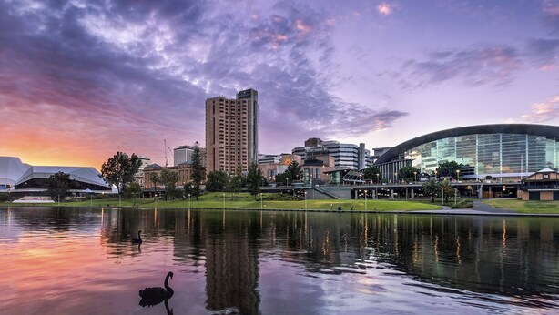 Un paisaje urbano con edificios modernos, un estadio grande y una masa de agua que refleja el cielo.