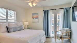 A bedroom with a large bed, a chair, a ceiling fan, and a view of the outside. - Uncrowded Corner Beachfront 3BR w/3 New Spa Baths (Gulf Shores)