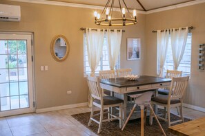 Uma sala de jantar com uma mesa de madeira, seis cadeiras, um candelabro e vista pela janela.