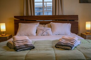 A neatly made bed with a striped towel and a starfish pillow, two bedside lamps, and a window with curtains. - The Nest Villa - Sleeps 16, 5BR Family Pool, Swings, BBQ, Gated Estate (Canaan, Tobago)