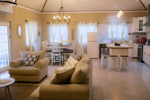 Una sala de estar con un sofá, un comedor con sillas y una cocina con un refrigerador y un lavamanos.