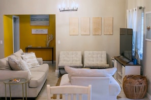 A living room with a sofa, armchairs, a coffee table, and a television. There is a wall with a painting and a sign. - The Nest Villa - Sleeps 16, 5BR Family Pool, Swings, BBQ, Gated Estate (Canaan, Tobago)