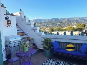 Enjoy breathtaking mountain views from this rooftop terrace, featuring a barbecue grill, comfortable seating, and lush greenery.