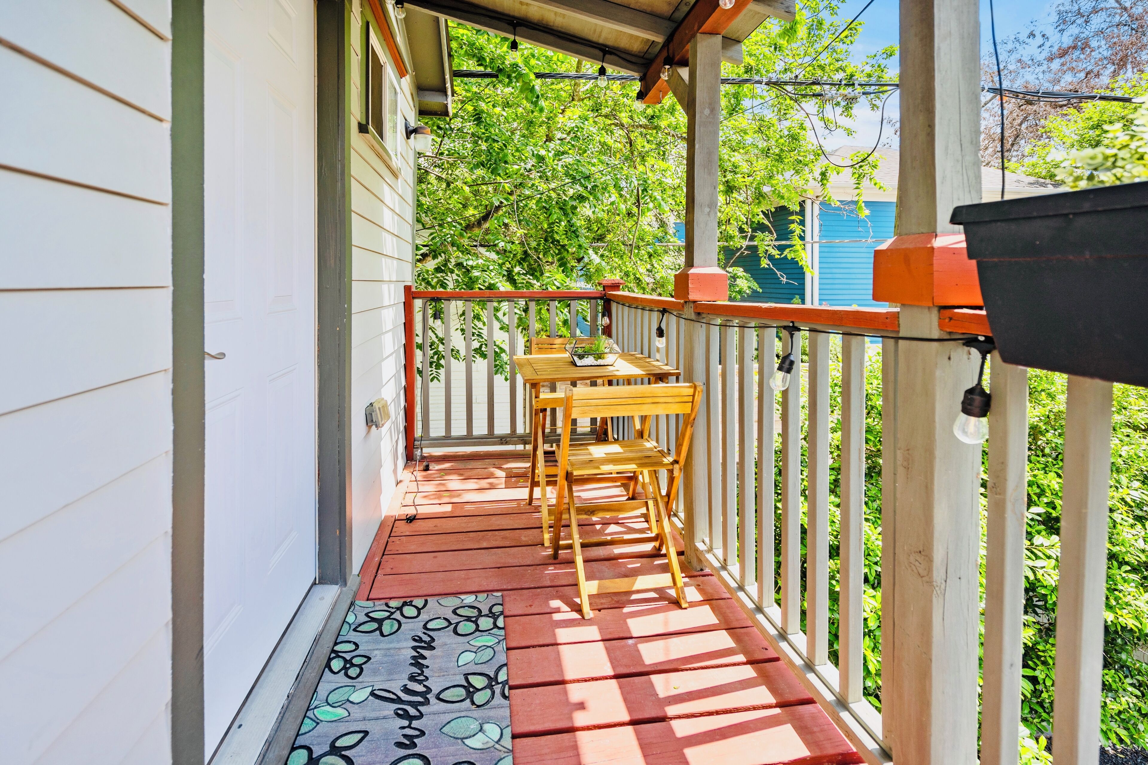 A wooden porch with a red and white railing, a wooden bench, and a welcome mat.