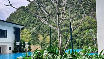 A modern building with a pool surrounded by lush greenery and a mountainous backdrop.