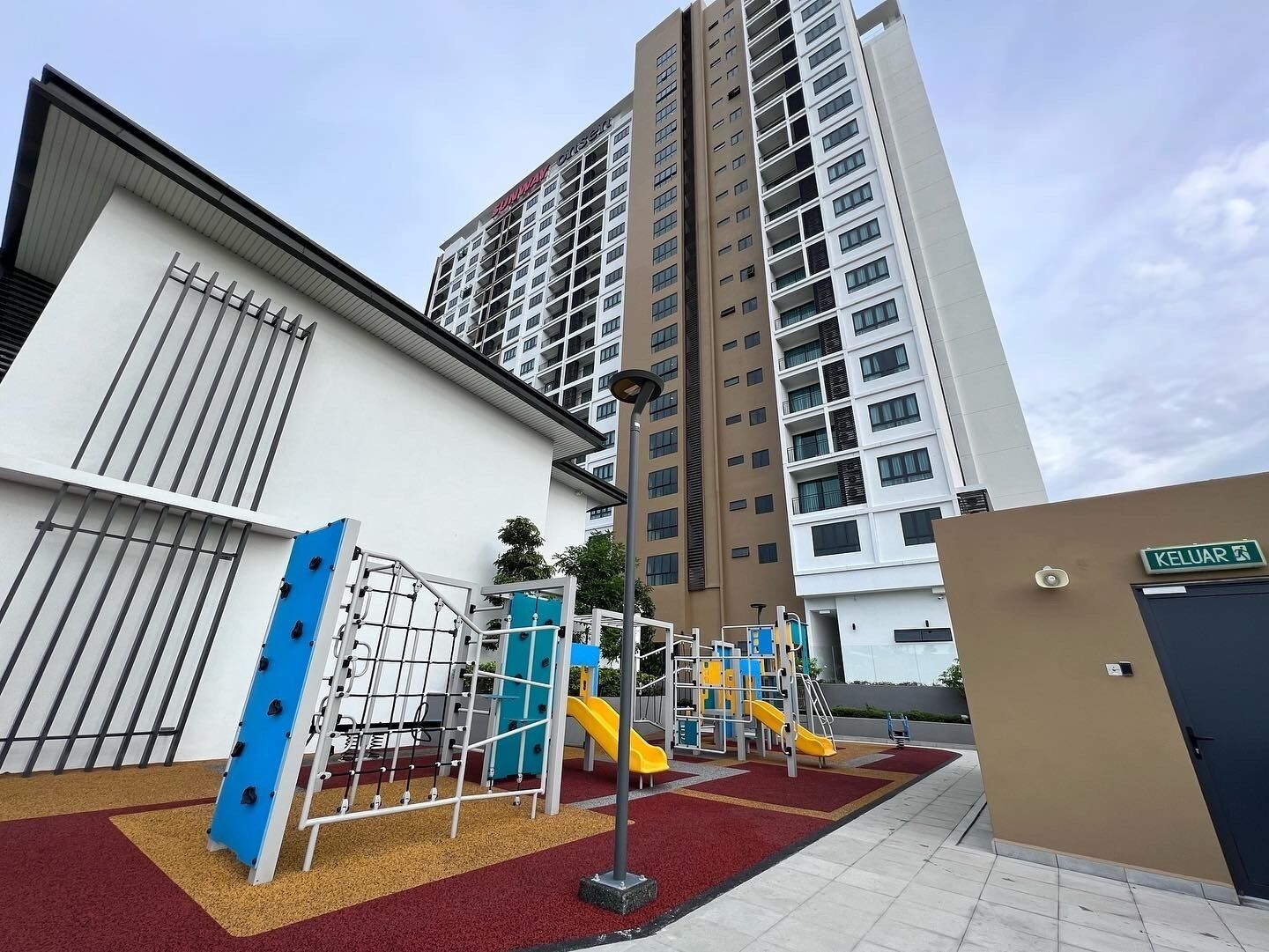 A playground with slides and climbing structures, adjacent to a building with a sign reading "KELUAR".