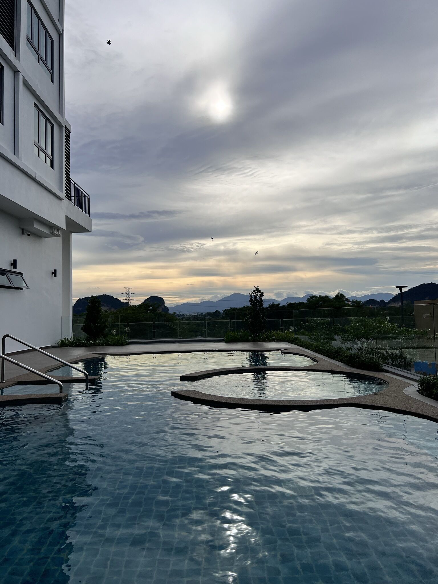 Une piscine avec vue sur les montagnes et un ciel nuageux.