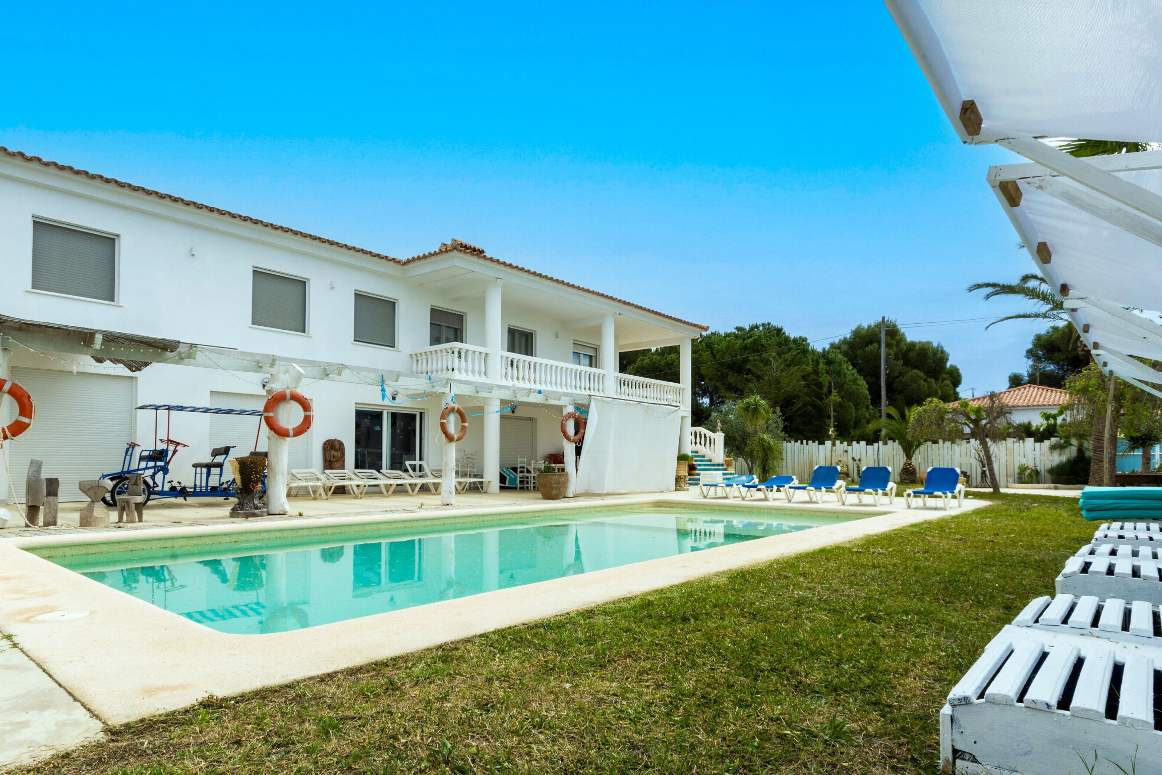 A pool area with a white building, blue lounge chairs, and a covered seating area.