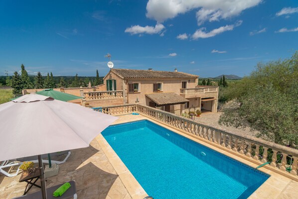Zona de piscina con una casa al fondo, cielo despejado y vistas al campo.