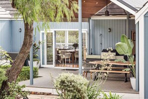 Eine überdachte Terrasse im Freien mit Essbereich, Grill und einer großen Pflanze im Topf.