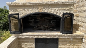 A stone fireplace with a brick interior, a black door below, and two open windows above. - Runaway Cottage Villa (Unesic)